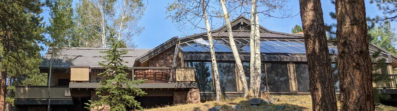 A large house nestled in the woods, featuring a prominent skylight on the roof and surrounded by tall trees.